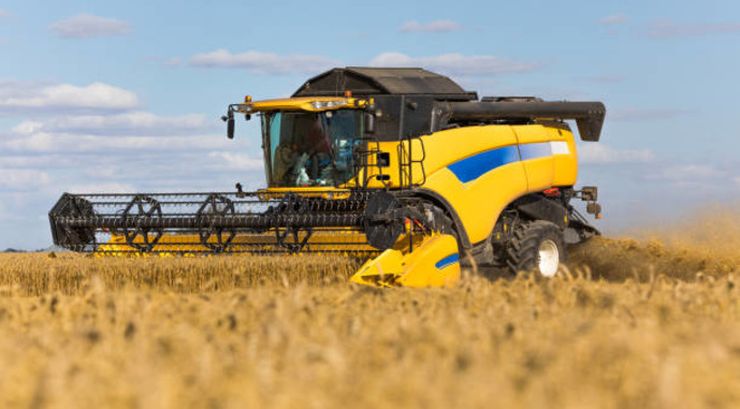 Yellow combine harvester on a wheat field with blue sky.